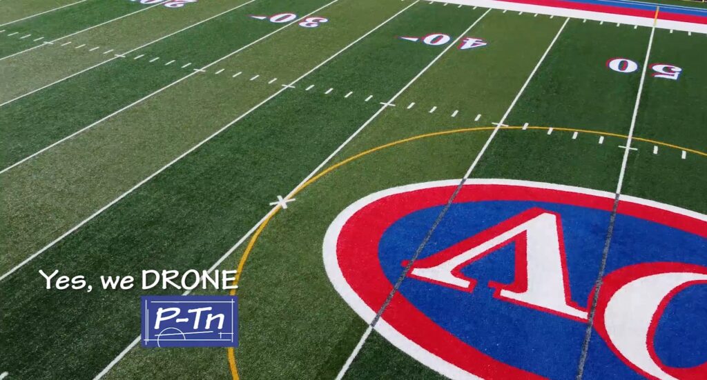 Drone still shot from video showing a shot from 10-30 feet off of the ground looking at a close up of a football field's turf | P-Tn