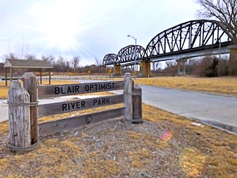 Wood sign says Blair Optimist River Park with bridge in the background | P-Tn