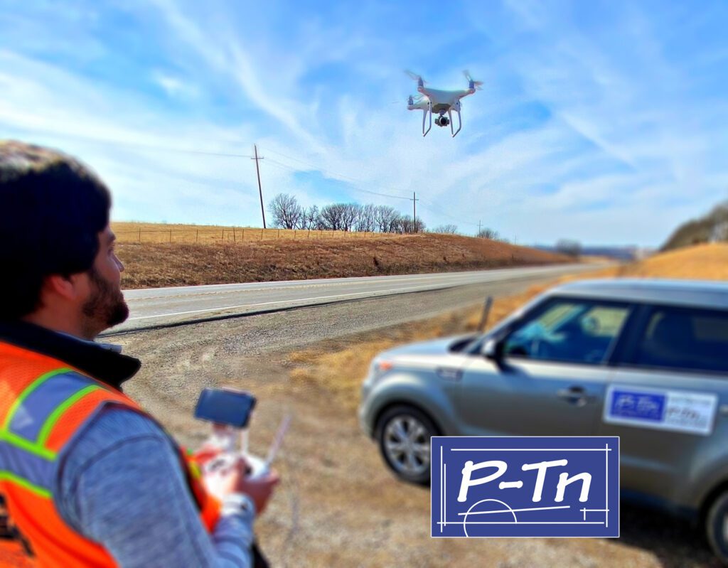 Man in construction orange vest flying a uas drone above a car with P-Tn logo. | P-Tn
