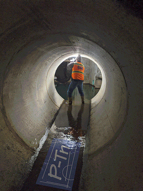 Man in orange vest in tunnel taking photo of underground sewage line | P-Tn