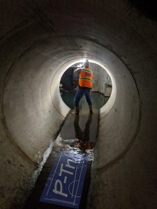 Man in orange vest in tunnel taking photo of underground sewage line | P-Tn